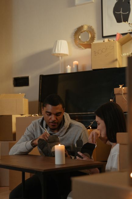 Inside a cardboard moving box viewed from above, containing a black and white household handbook with images of living room furniture, decorative items, and interior spaces on its cover. The box is situated on a light wooden floor, with no other objects visible. The handbook appears to be part of packing and planning materials used during a home relocation process, highlighting the importance of organized packing when arranging furniture transport or removals. This setup is typical in professional house removals, where packing materials such as cardboard boxes and printed guides are used by movers from Movers Hounslow to ensure a smooth and efficient moving process, especially when avoiding common mistakes during bookings in Hounslow.